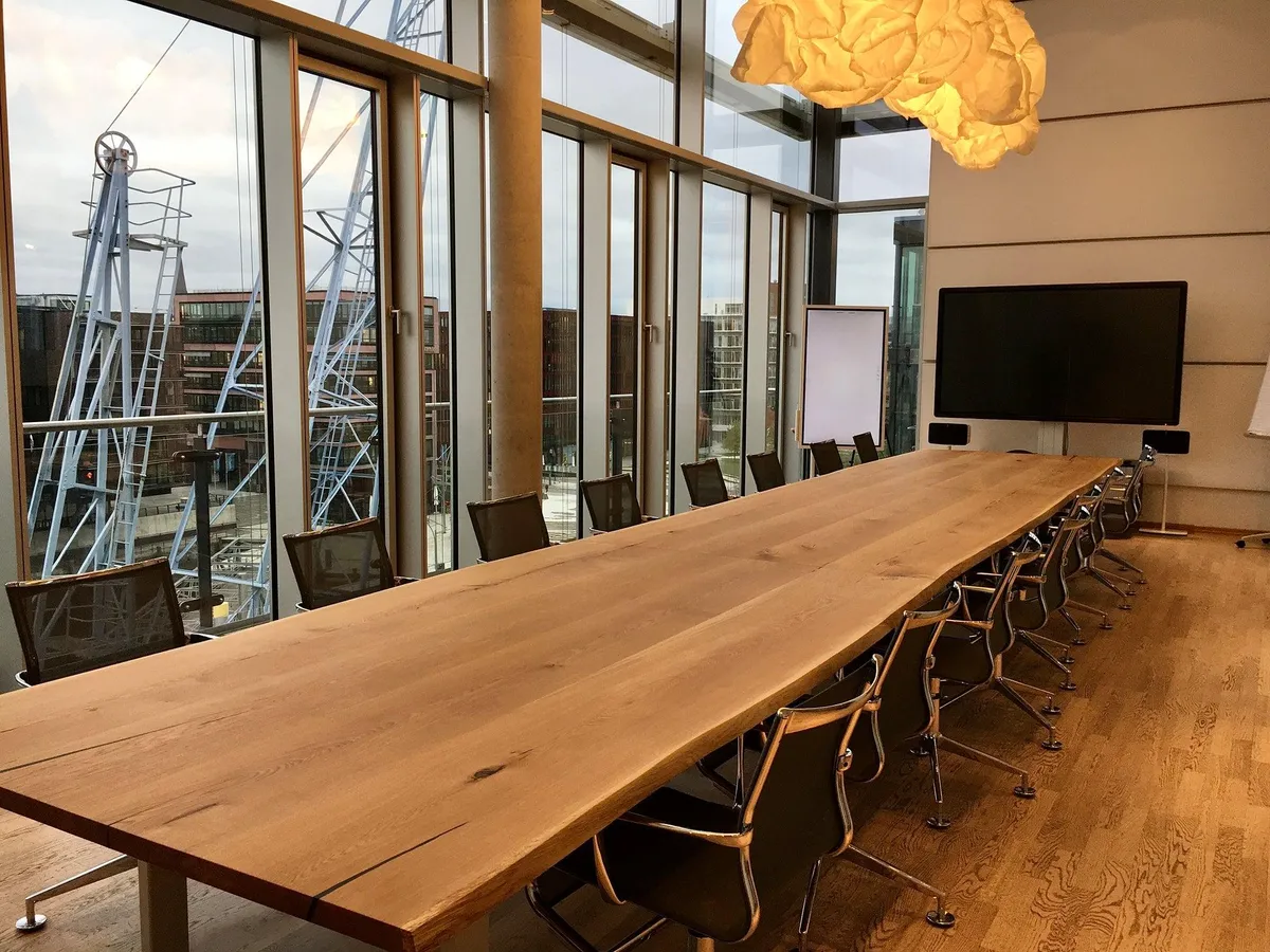 A meeting room with a long wooden table and office chairs by large windows