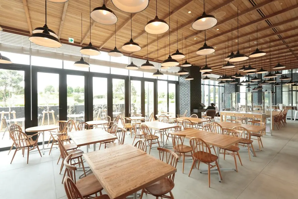 A bright dining room with wooden tables and chairs under rows of pendant lamps